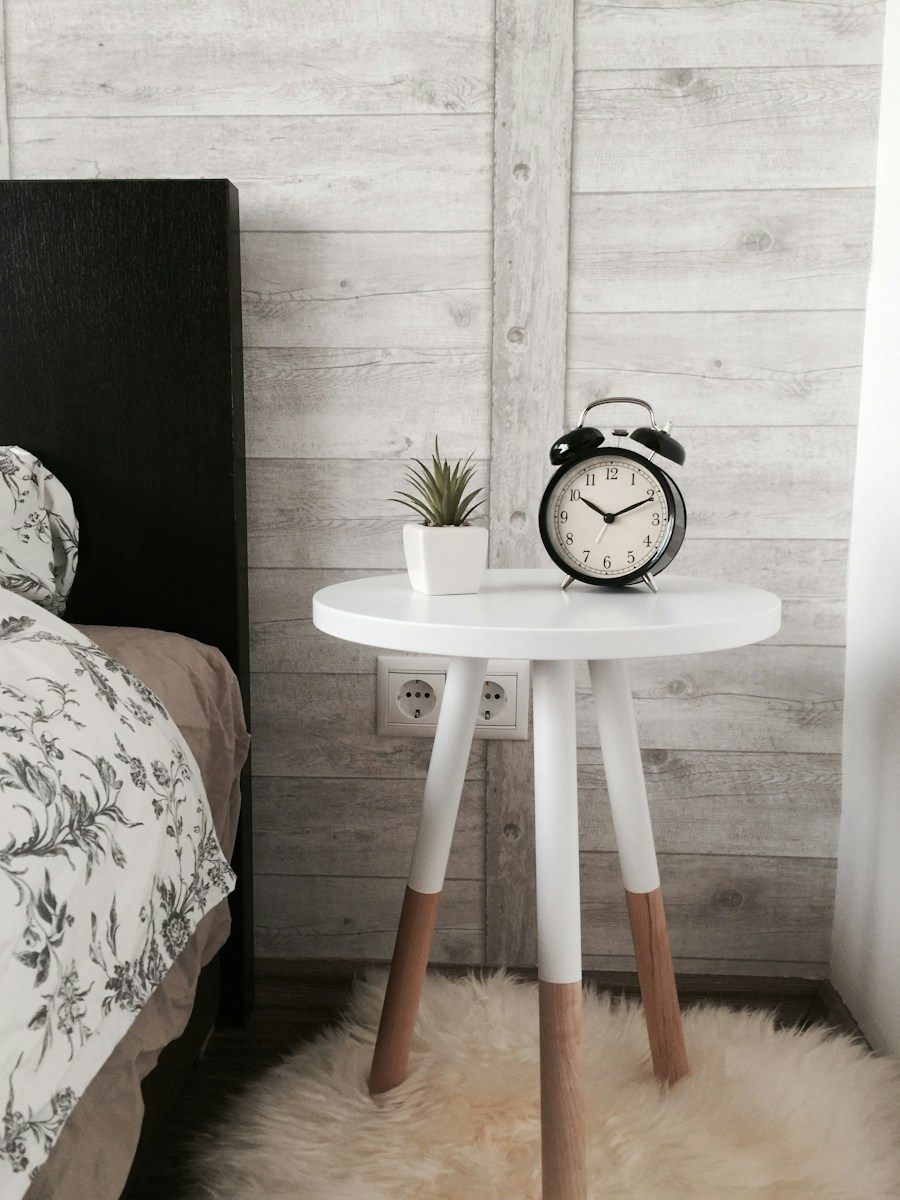 A round white bedside table on three white and wood legs