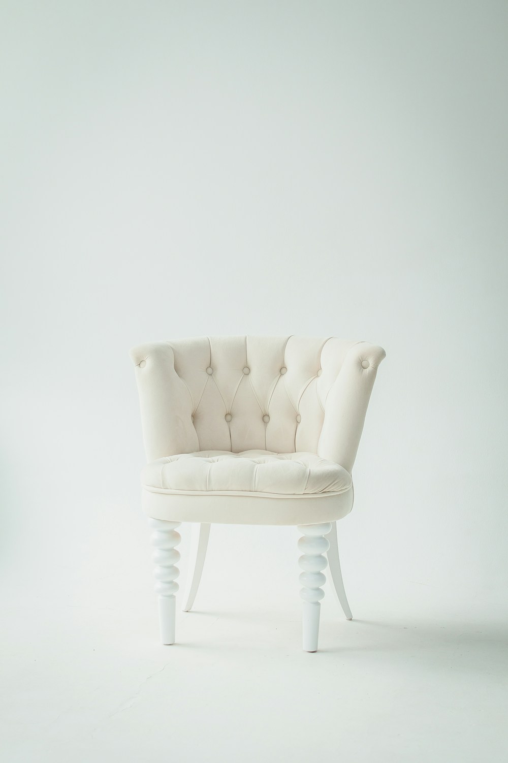 An ivory upholstered chair with a curved, button-tufted back