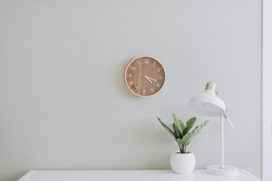 A white desk lamp with brass details beside a plant and wall clock