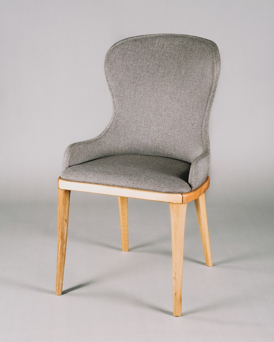A grey upholstered dining chair with light wooden legs