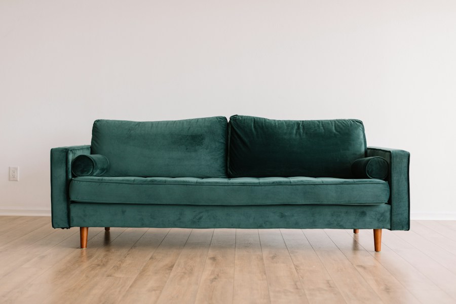 A green velvet sofa with cylindrical cushions and wooden legs