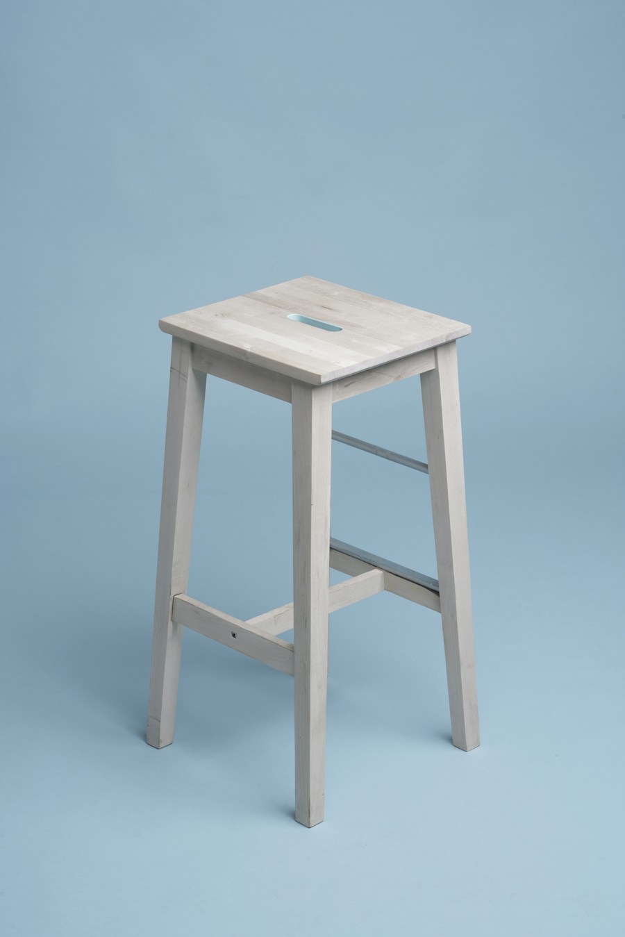 A pale wooden counter stool with a square seat against a blue wall