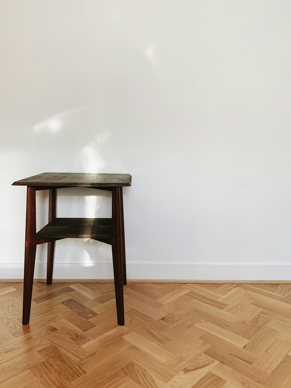 A dark wooden side table with a lower shelf on a parquet floor